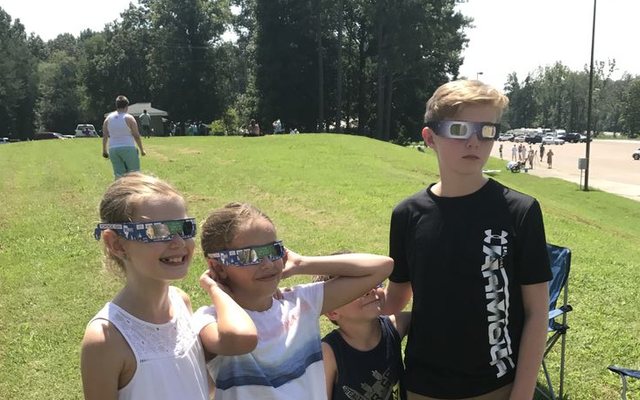Four children in cardboard eclipse glasses standing in a grassy field