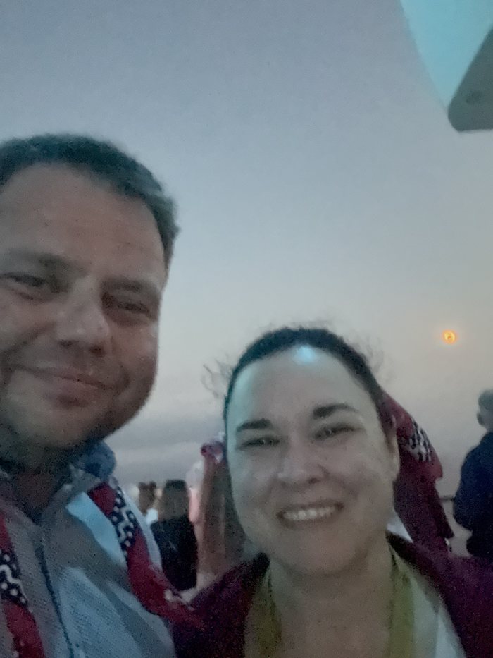 Two people smiling on deck during totality, the eclipsed sun visible behind them